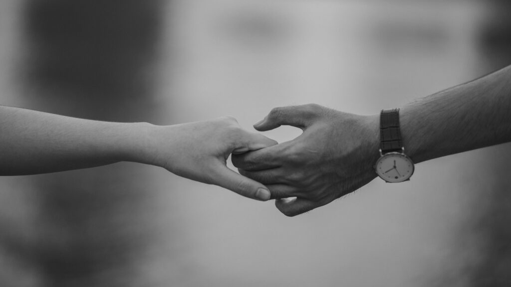 Dlaczego boisz się odejść, nawet gdy wiesz, że powinnaś? Monochrome image of two hands holding, symbolizing love and connection.