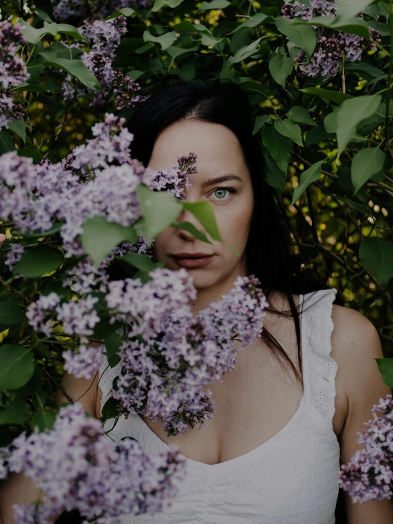 Nie jesteś zmęczona życiem. Jesteś zmęczona udawaniem. Captivating portrait of a woman surrounded by vibrant lilac flowers in a lush spring garden.