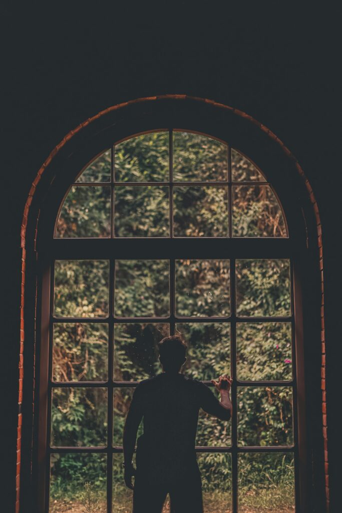 Uratować związek czy siebie? Jak podjąć świadomą decyzję. Silhouette of a man standing at an arched window with lush greenery outside, creating a serene and contemplative scene.