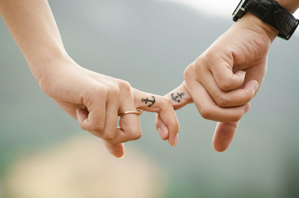 Dlaczego wciąż wracam do tego samego schematu w związku? Close-up of a couple holding hands, featuring anchor tattoos symbolizing love and connection.