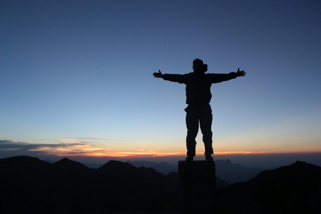 Dlaczego boję się sukcesu i się wycofuję? Mechanizm lęku przed wielkością. Back view of unrecognizable male traveler with outstretched arms enjoying sunset and nature on mountain peak