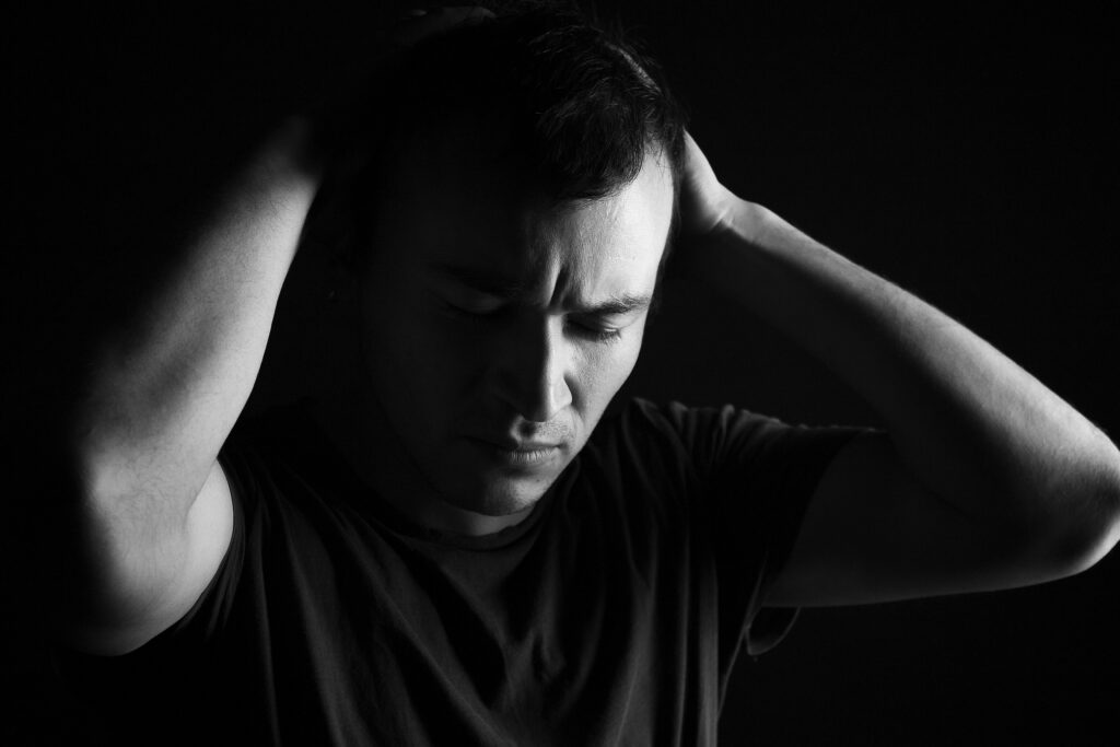 Mam wszystko i nadal jestem nieszczęśliwy – Dlaczego sukces nie daje radości? A black and white portrait capturing a distressed man with hands on head, conveying anxiety.